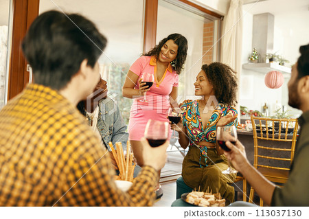 Smiling friends enjoying in conversation and drinking wine during festive dinner at home party 113037130
