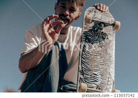 Close up of male skater looking on something while sitting with skateboard on a ramp 113037142