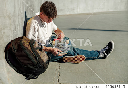 Young man repairing his skateboard in the skate park use special key. High quality photo Young man repairing his skateboard in the skate park use special key. High quality photo 113037145