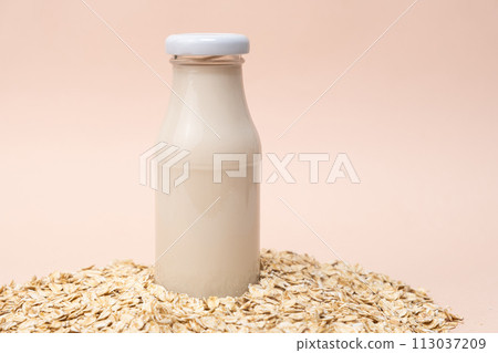 Oat milk in a glass bottle among dry oatmeal flakes on a beige background. Oat milk in a glass bottle among dry oatmeal flakes on a beige background. 113037209