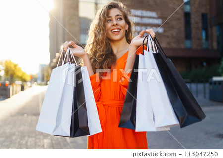 Stylish woman with shopping bag walking at sunny street in bright dress. Concept of sales, discounts 113037250