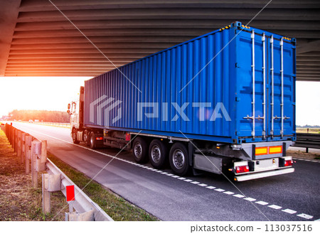 A container truck with a semi-trailer transports cargo from a port to another country along a highway in the summer against the backdrop of the sun. Logistics in cargo transportation, business 113037516