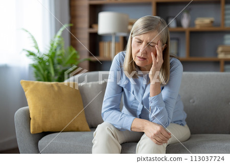 An elderly woman appears distressed and alone, sitting pensively on a couch in a well-lit living room, evoking emotions of loneliness and concern. An elderly woman appears distressed and alone, sitting pensively on a couch in a well-lit living room, evoking emotions of loneliness and concern. 113037724