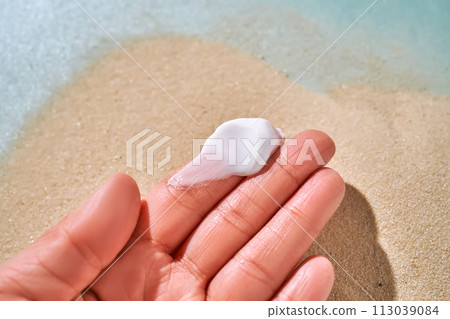 A smear of white cream with SPF on the fingers against a background of sand. A smear of white cream with SPF on the fingers against a background of sand. 113039084