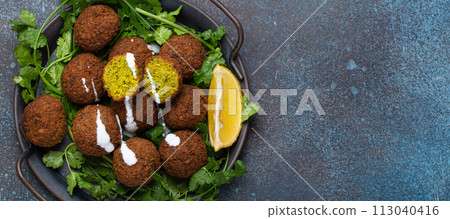 Plate of fried falafel balls served with fresh green cilantro and lemon top view on rustic concrete background. Traditional vegan dish of Middle Eastern cuisine, copy space Plate of fried falafel balls served with fresh green cilantro and lemon top view on rustic concrete background. Traditional vegan dish of Middle Eastern cuisine, copy space 113040416