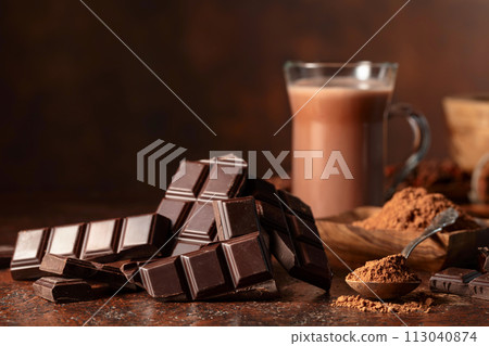 Pieces of bitter chocolate and glass of cocoa drink on a brown table. Pieces of bitter chocolate and glass of cocoa drink on a brown table. 113040874