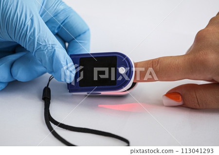 Doctor examining patient with fingertip pulse oximeter in bed, closeup 113041293