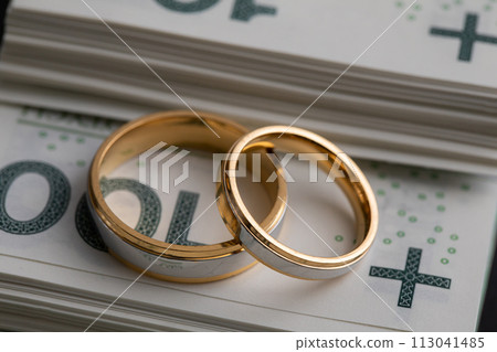 Gold wedding rings surrounded by a stack of Polish banknotes. 113041485
