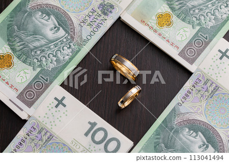 Gold wedding rings surrounded by a stack of Polish banknotes. Gold wedding rings surrounded by a stack of Polish banknotes. 113041494