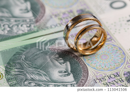 Gold wedding rings surrounded by a stack of Polish banknotes. 113041506