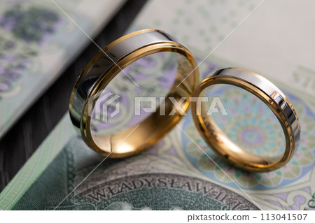 Gold wedding rings surrounded by a stack of Polish banknotes. Gold wedding rings surrounded by a stack of Polish banknotes. 113041507