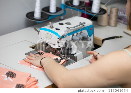 A young schoolgirl learns to sew face masks during a pandemic on an overlock sewing machine. A young schoolgirl learns to sew face masks during a pandemic on an overlock sewing machine. 113041654
