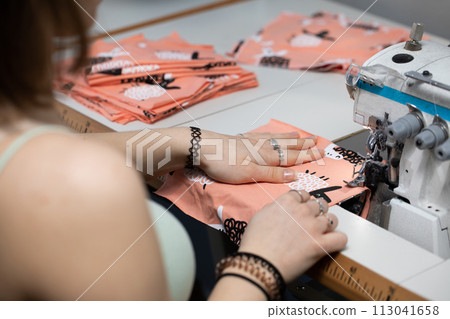 A young schoolgirl learns to sew face masks during a pandemic on an overlock sewing machine. 113041658