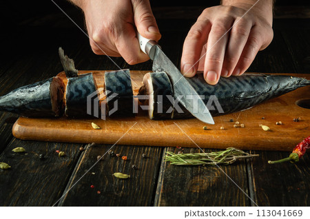 Chef preparing fresh mackerel on the kitchen table. Low key concept for preparing a fish dish. Slicing Scomber fish with a knife 113041669