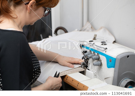 Experienced seamstress sews pillow covers on a sewing machine called overlock. 113041691