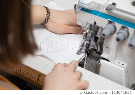 A teenager sews a brown dress on a sewing machine called an overlock. A teenager sews a brown dress on a sewing machine called an overlock. 113041695