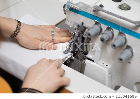 A teenager sews a brown dress on a sewing machine called an overlock. A teenager sews a brown dress on a sewing machine called an overlock. 113041699