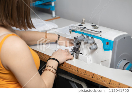 A teenage schoolgirl learns to sew protective masks on an overlock during a pandemic. A teenage schoolgirl learns to sew protective masks on an overlock during a pandemic. 113041700