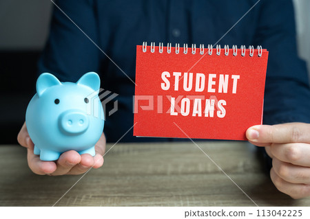 Student loans concept. Financial aid provided to students to help cover the cost of higher education. Note in male hands and pig piggy bank 113042225