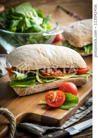 Ciabatta sandwich with arugula salad, bacon and yellow cheese. 113042456