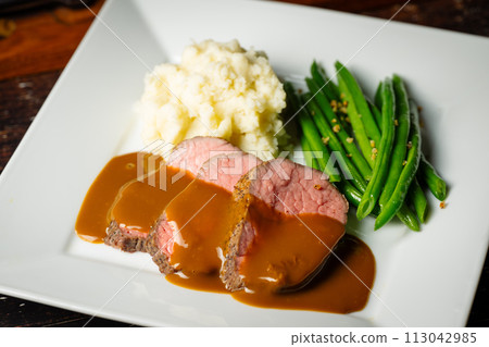 pouring brown gravy sauce on roasted beef pouring brown gravy sauce on roasted beef 113042985