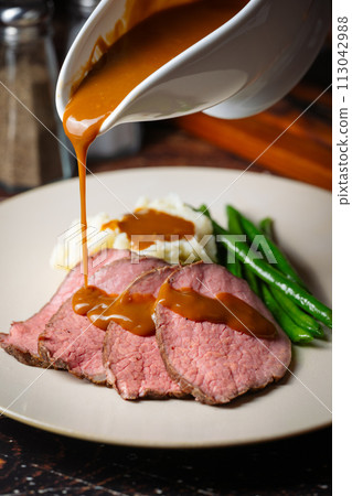 pouring brown gravy sauce on roasted beef 113042988