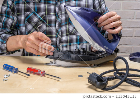 master repairs the iron in the workshop on the table using tools master repairs the iron in the workshop on the table using tools 113043115