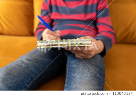 Rest between classes. boy draws in a notebook while sitting on sofa. Homework 113043154
