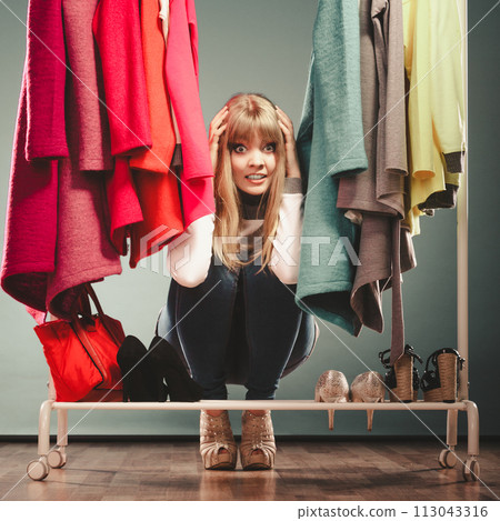 Scared woman hiding among clothes in mall wardrobe 113043316