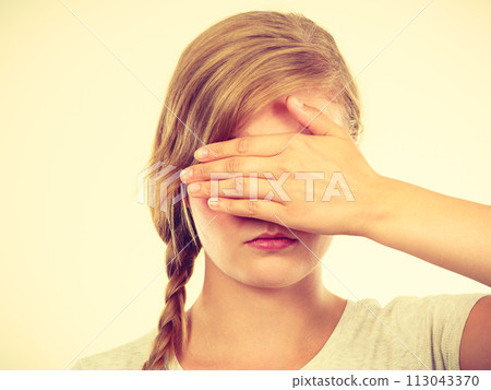 Shy teenage girl hiding face behind hand 113043370