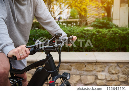 Close-up man riding electric bike at sunset. Bike sharing city service. Man renting eco urban public transport 113043591