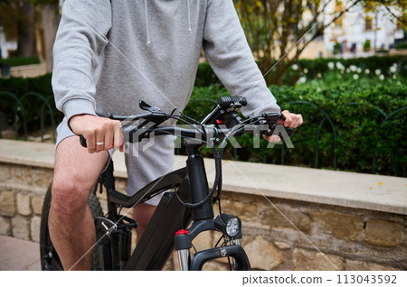 Close-up of a man cyclist riding an electric bike, bicycle in the city street. Bike sharing city service. Copy ad space Close-up of a man cyclist riding an electric bike, bicycle in the city street. Bike sharing city service. Copy ad space 113043592