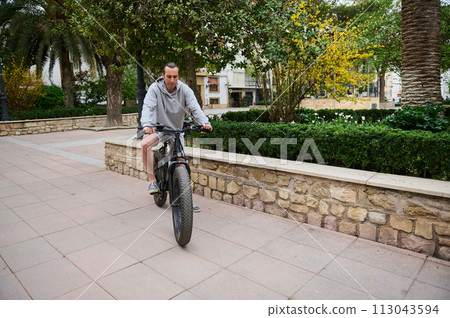 Full length portrait of a handsome Caucasian man renting electric bike, riding in the city. Bike sharing city service Full length portrait of a handsome Caucasian man renting electric bike, riding in the city. Bike sharing city service 113043594