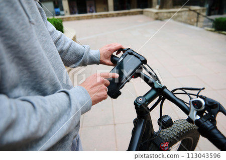 Close-up cyclist checks mobile app on smartphone Mockup digital touch screen, setting up a route on internet online map Close-up cyclist checks mobile app on smartphone Mockup digital touch screen, setting up a route on internet online map 113043596