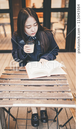 A high school girl reading a book while drinking a drink at an outdoor cafe seat A high school girl reading a book while drinking a drink at an outdoor cafe seat 113043984