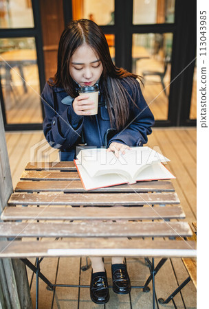 A high school girl reading a book while drinking a drink at an outdoor cafe seat A high school girl reading a book while drinking a drink at an outdoor cafe seat 113043985