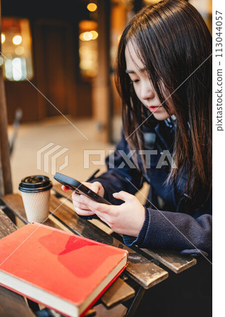High school girl playing with a smartphone while drinking a drink at a cafe 113044057