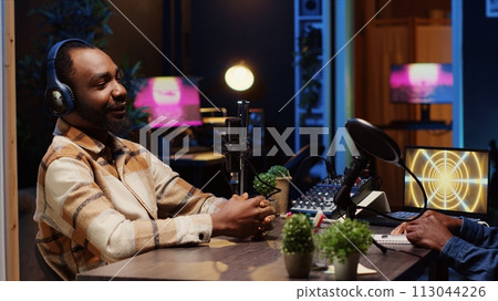 Man hosting podcast, using professional audio equipment to ensure high sound quality during live discussion with guest. Internet show presenter talking with man with 3D animation running in background Man hosting podcast, using professional audio equipment to ensure high sound quality during live discussion with guest. Internet show presenter talking with man with 3D animation running in background 113044226