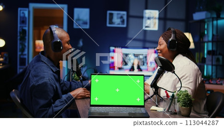Focus on green screen laptop in front of show host recording podcast, using analog mixer in studio. Mockup notebook and man setting up audio devices in live broadcast for flawless sound quality 113044287