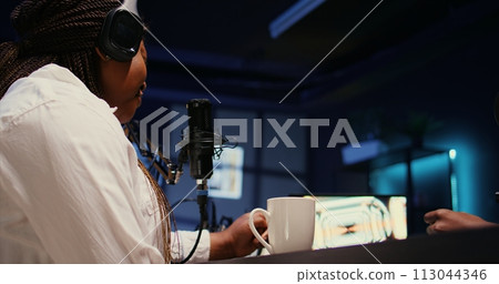 Woman laughing and enjoying cup of coffee during comedy focused podcast, entertained by funny man. Guest amused by talking show host telling jokes to her and audience watching at home Woman laughing and enjoying cup of coffee during comedy focused podcast, entertained by funny man. Guest amused by talking show host telling jokes to her and audience watching at home 113044346