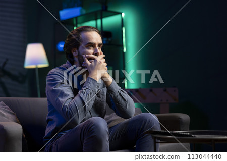 Man covering mouth in shock watching horror movie on streaming services, having relaxing evening. Viewer in apartment gasping at violent graphic film scene, surprised by plot events 113044440