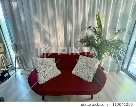 Interior of a living room with red sofa and white pillows in front of the window with plant Interior of a living room with red sofa and white pillows in front of the window with plant 113045296