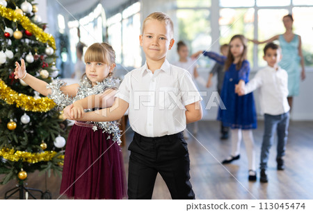 Little children standing in pairs in school-hall decorated with Xmas tree Little children standing in pairs in school-hall decorated with Xmas tree 113045474