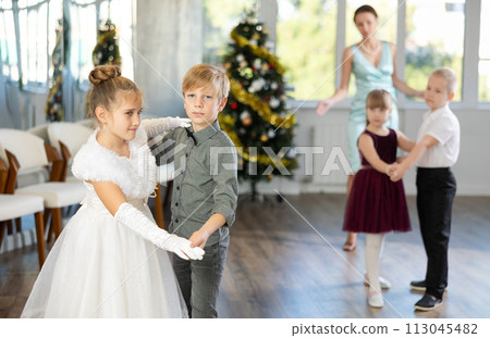 Christmas ball - group of preteen children in festive clothes dances a foxtrot near New Year tree 113045482