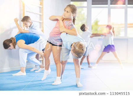 Children practicing in pair self-defence movements with female trainer supervision 113045515