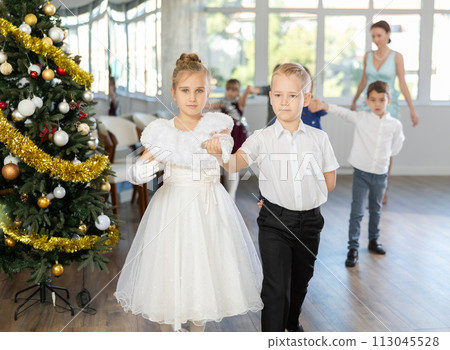 Group of preteen children in festive clothes dances waltz around Christmas tree 113045528