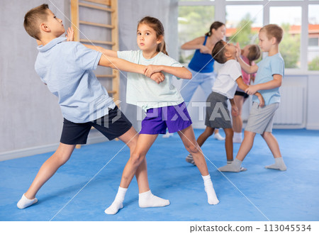 Children practicing in pair self-defence movements with female trainer supervision 113045534