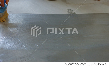 Builder painter primer concrete floor. Worker preparing the floor under painting. 113045674