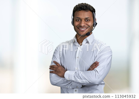 Portrait of male call center agent looking at camera with crossed arms. Call center operator on blurred background. Portrait of male call center agent looking at camera with crossed arms. Call center operator on blurred background. 113045932
