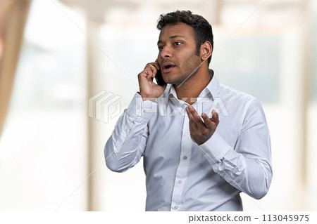 Serious young businessman talking to someone on mobile phone. Blur interior background. 113045975